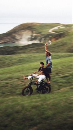 two people riding on the back of a dirt bike while another person holds up a frisbee