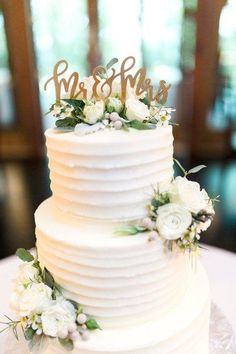 a white wedding cake with flowers and the word mr and mrs on top is sitting on a table