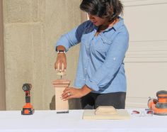 a woman sanding down a piece of wood on top of a table with tools