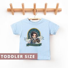 Introducing our "Saint Joan of Arc" Toddler Shirt, a delightful piece of Catholic toddler apparel celebrating St. Joan of France. This shirt highlights the bravery and devotion of this revered saint, making it a meaningful gift for young children. Crafted from soft, high-quality fabric, this comfortable shirt is perfect for everyday wear or special occasions. It's an ideal baptism gift or thoughtful present for any occasion, honoring the legacy of Saint Joan of Arc and her role among Catholic sa Saint Joan Of Arc, St Joan, Jeanne D'arc, Joan Of Arc, Toddler Sizes, Toddler Gifts, Toddler Outfits, Kids Tshirts, Quality Fabric