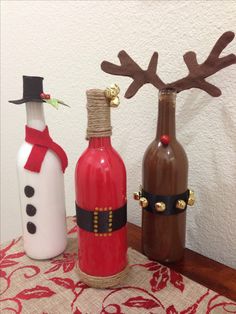 three wine bottles decorated to look like snowmen with antlers on their heads and noses