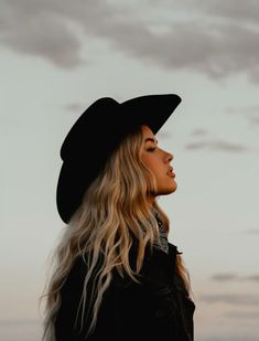 a woman with long blonde hair wearing a black hat and looking off into the distance