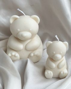 two small white teddy bears sitting next to each other on a bed covered in white sheets