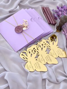 purple and gold wedding stationery on a white bed with lavender flowers in the background