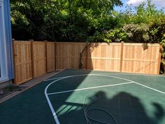 an empty basketball court in front of a wooden fence with a shadow on the ground