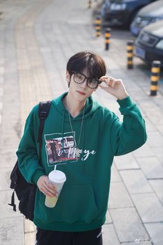 a young man with glasses and a green hoodie is holding a drink in his hand