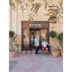 two people sitting at tables in front of a sufta restaurant with potted plants