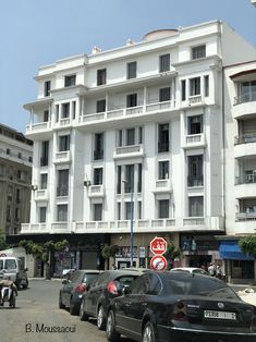 cars are parked on the street in front of a white building with balconies