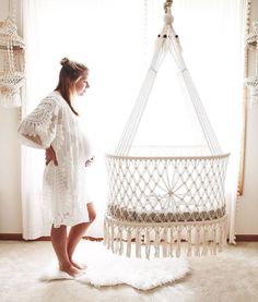 a pregnant woman standing in front of a white crib with tassels hanging from it