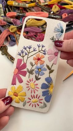 a woman is holding a phone case with flowers on it and crochet needles