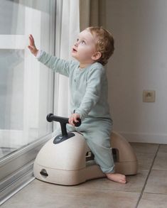 a little boy sitting on top of a toy car looking out the window at something outside