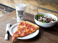 a slice of pizza on a plate next to a bowl of salad and a drink