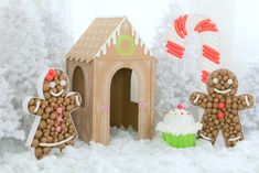 two gingerbread men are standing in front of a ginger house and cupcakes