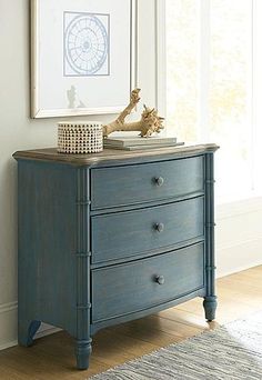 a blue dresser sitting in front of a window next to a painting on the wall