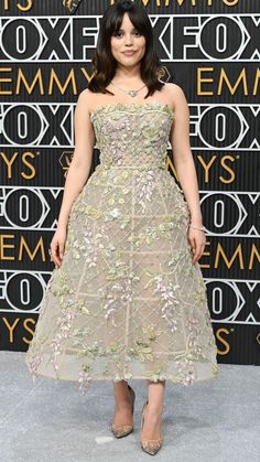 a woman in a dress and heels standing on a gray carpet with an embellished wall behind her