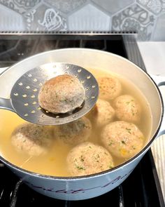 a ladle full of soup with meatballs in it on top of the stove