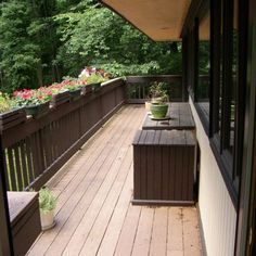 a wooden deck with benches and potted plants on the top level, overlooking trees