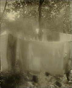 an old photo of a man washing his clothes in the yard with trees behind him