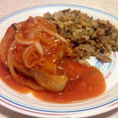 a white plate topped with meat covered in gravy next to rice and veggies