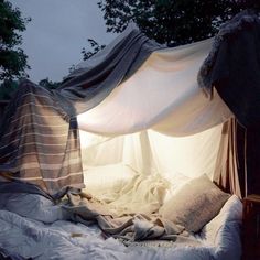 an unmade bed with white sheets and blankets on it's sides, in front of trees