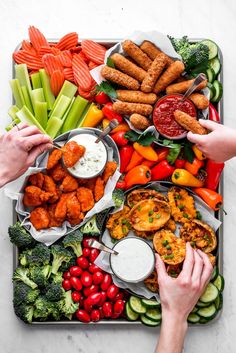 two hands reaching for dipping sauce on a platter filled with vegetables and meats