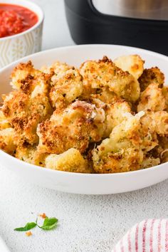 a white bowl filled with fried food next to a slow cooker and red sauce