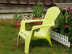 a yellow plastic lawn chair sitting on top of a lush green grass covered yard next to potted plants