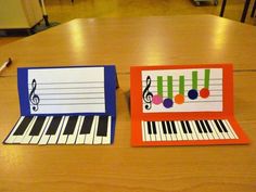 two cards with musical notes on them sitting on a table next to a piano keyboard