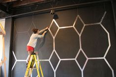 a man on a ladder painting a wall with white hexagonal net behind him