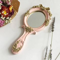 a pink vanity mirror sitting on top of a table next to flowers and a vase