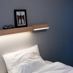 a bed with white linens and a wooden shelf above it that is lit up