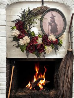 a fireplace decorated with flowers and brooms next to an old fashioned photo on the wall