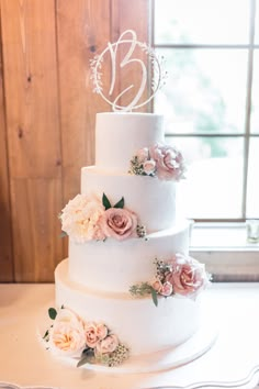 a white wedding cake with pink flowers on the side and a monogram topper