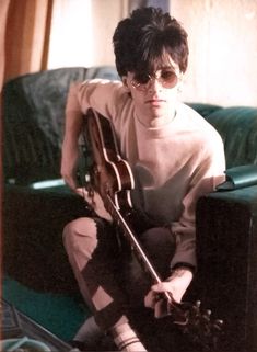 a person sitting on a couch with a guitar in their lap and wearing sunglasses,