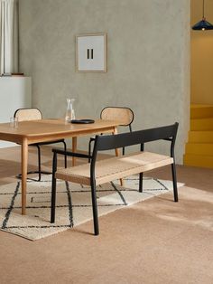 a wooden table with two chairs and a bench in front of it on a carpeted floor