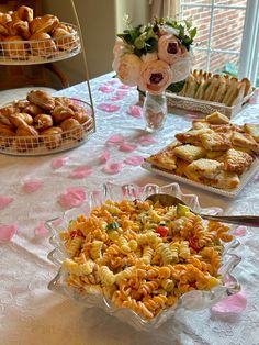 a table topped with trays of food next to a vase filled with pink flowers