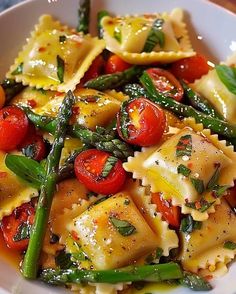 pasta with asparagus, tomatoes and spinach in a white bowl on a table