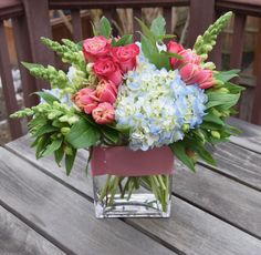 a glass vase filled with pink and blue flowers on top of a wooden table next to a fence