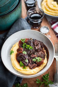 a bowl filled with meat and sauce on top of a wooden table next to other dishes