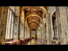 an ornate hallway with many tables and benches in it, along with intricate paintings on the walls