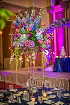 a tall vase filled with lots of purple and blue flowers on top of a table