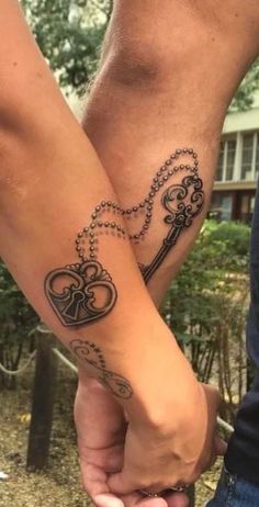 two people holding hands with key tattoos on their arms and the other hand has a heart shaped