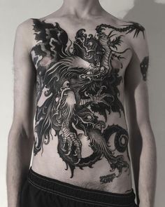 a man with a dragon tattoo on his chest is standing in front of a white wall