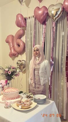 a woman standing next to a table filled with cakes and balloons