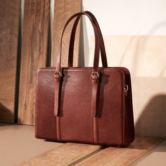 a brown leather bag sitting on top of a wooden floor next to a wall with wood planks