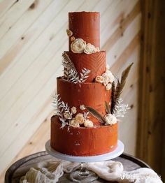 a three tiered cake decorated with flowers and feathers on top of a wooden table