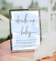 a drink up baby sign sitting on top of a wooden table next to a feather