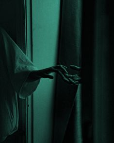 a person's hand reaching out from behind a curtain in a dark room with green light