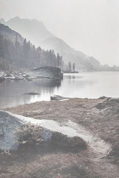 a lake surrounded by mountains and trees on a foggy day