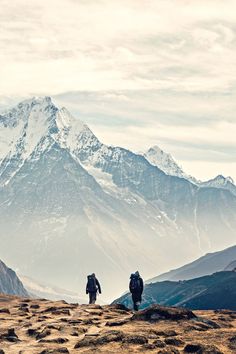 two people walking up a hill with mountains in the backgrouds behind them